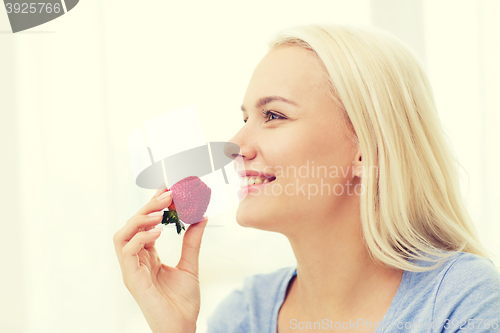 Image of happy woman eating strawberry at home