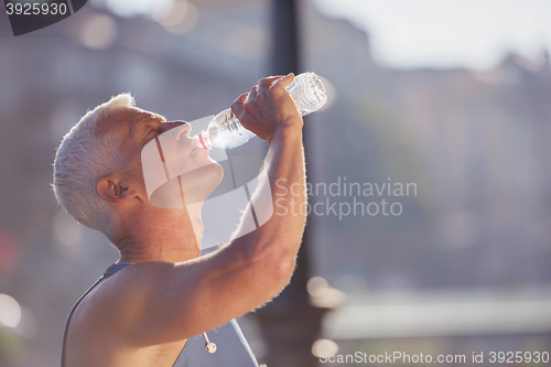 Image of senior jogging man drinking fresh water from bottle