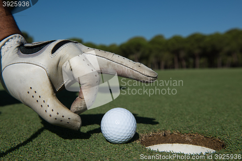 Image of man\'s hand putting golf ball in hole