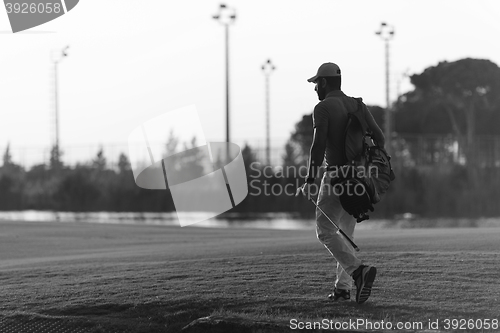 Image of golfer  walking and carrying golf  bag at beautiful sunset