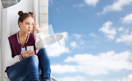 Image of teenage girl sitting on windowsill with smartphone