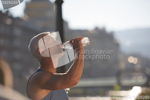 Image of senior jogging man drinking fresh water from bottle