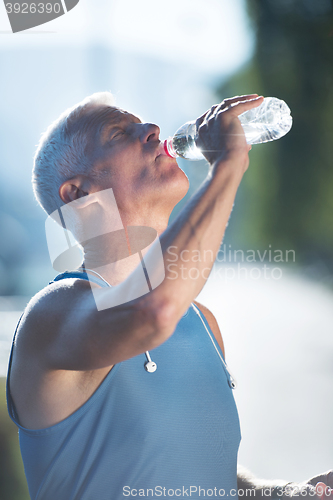 Image of senior jogging man drinking fresh water from bottle