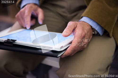 Image of Closeup of mature hands holding tablet.
