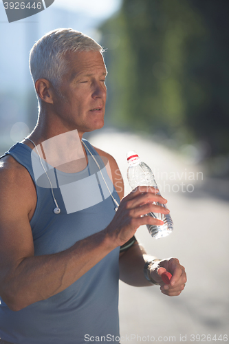 Image of senior jogging man drinking fresh water from bottle