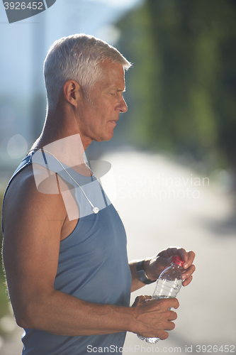 Image of senior jogging man drinking fresh water from bottle