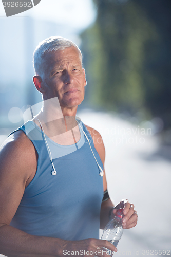 Image of senior jogging man drinking fresh water from bottle