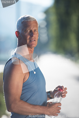 Image of senior jogging man drinking fresh water from bottle