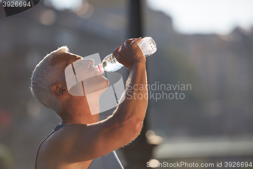 Image of senior jogging man drinking fresh water from bottle