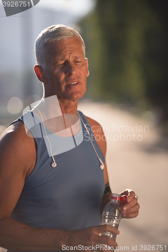 Image of senior jogging man drinking fresh water from bottle