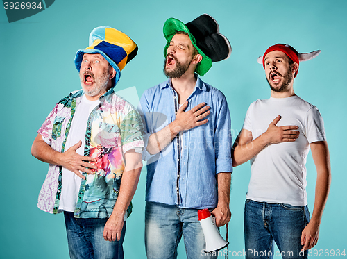 Image of The three football fans singing the national anthem over blue