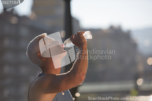 Image of senior jogging man drinking fresh water from bottle