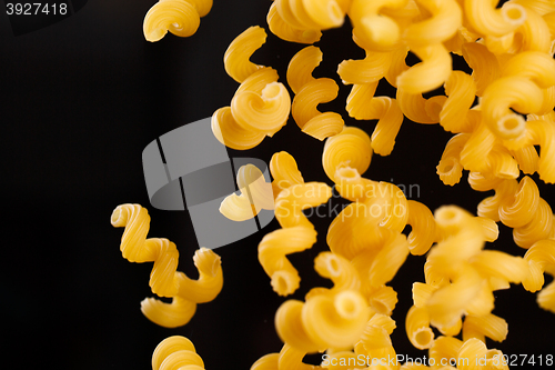 Image of Falling cavatappi pasta. Flying yellow raw macaroni over black background. 