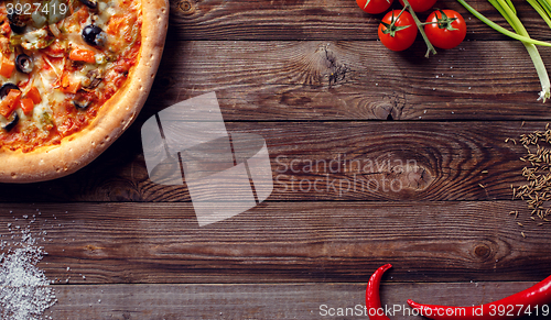 Image of Italian pizza with tomatoes on a wooden table, top view.