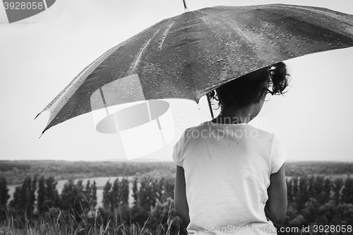 Image of girl sitting in the pouring rain with an umbrella