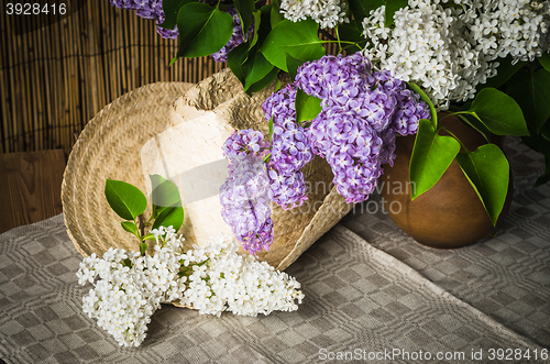 Image of Still-life with a bouquet of lilacs and a straw hat, close-up
