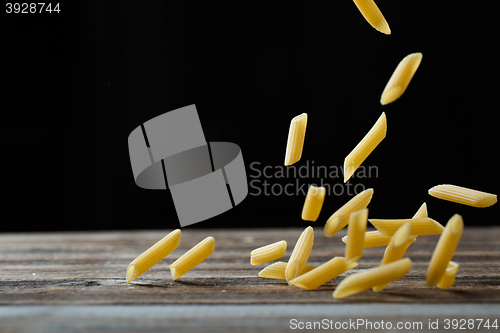 Image of Falling penne pasta. Flying yellow raw macaroni over black background.