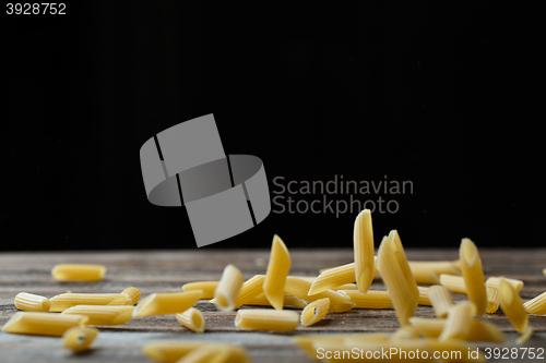 Image of Falling penne pasta. Flying yellow raw macaroni over black background.