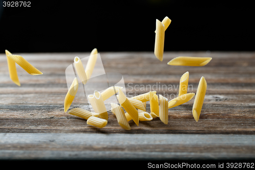 Image of Falling penne pasta. Flying yellow raw macaroni over black background.