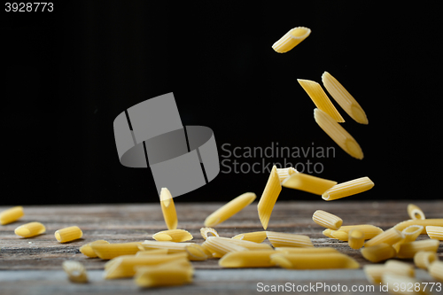 Image of Falling penne pasta. Flying yellow raw macaroni over black background.