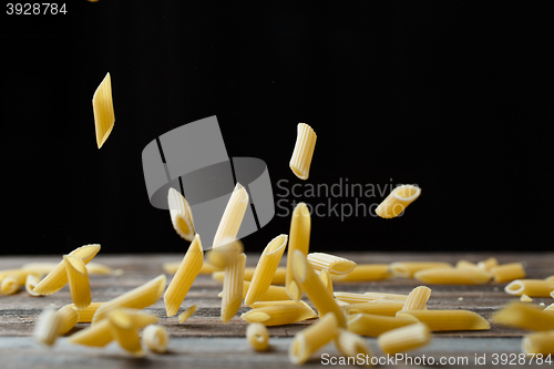 Image of Falling penne pasta. Flying yellow raw macaroni over black background.