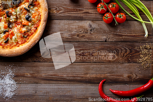 Image of Italian pizza with tomatoes on a wooden table, top view.