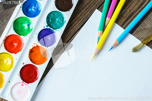 Image of Art tools. Watercolor Paints and brushes with blank white paper  on wooden background close up.