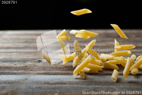 Image of Falling penne pasta. Flying yellow raw macaroni over black background.