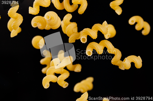 Image of Falling cavatappi pasta. Flying yellow raw macaroni over black background. 