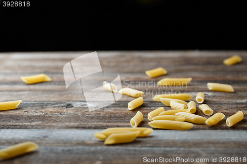 Image of Falling penne pasta. Flying yellow raw macaroni over black background.