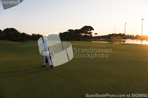 Image of golfer  walking and carrying golf  bag at beautiful sunset