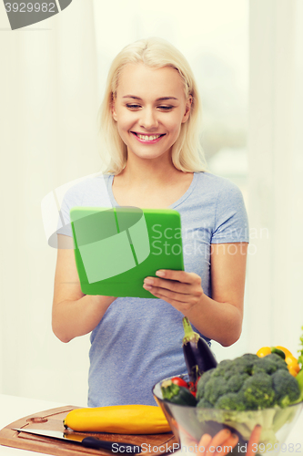 Image of smiling young woman with tablet pc cooking at home