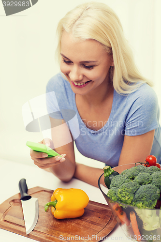 Image of smiling woman with smartphone cooking vegetables