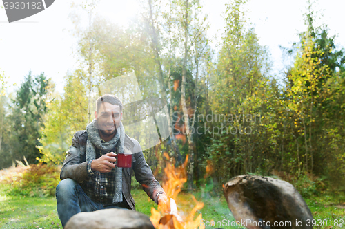Image of happy man drinking hot tea near camp fire