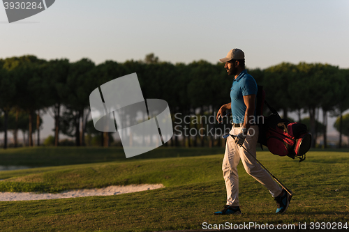 Image of golfer  walking and carrying golf  bag at beautiful sunset