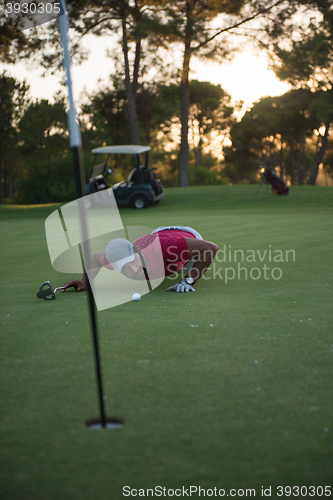 Image of golf player blowing ball in hole with sunset in background