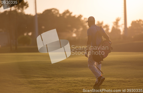 Image of golfer  walking and carrying golf  bag at beautiful sunset