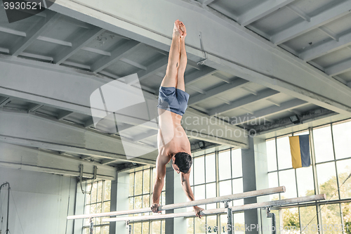 Image of Male gymnast performing handstand on parallel bars