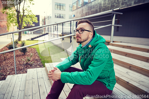 Image of happy young hipster man sitting on stairs in city