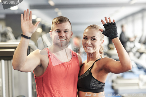 Image of smiling man and woman waving hands in gym