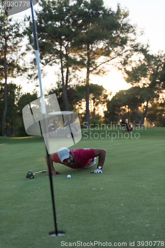 Image of golf player blowing ball in hole with sunset in background