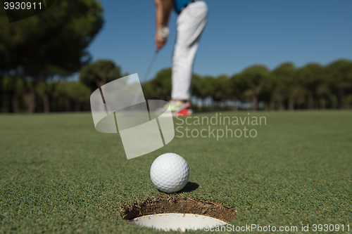 Image of golf player hitting shot, ball on edge of hole