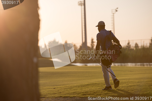 Image of golfer  walking and carrying golf  bag at beautiful sunset