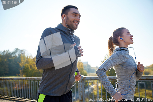 Image of happy couple with earphones running outdoors