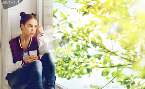 Image of teenage girl sitting on windowsill with smartphone