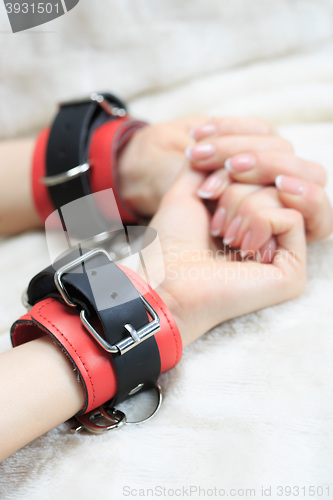 Image of female hands in leather handcuffs. on the background sheet. sex toys.