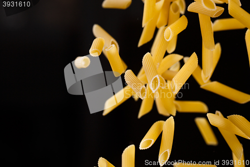 Image of Falling penne pasta. Flying yellow raw macaroni over black background.