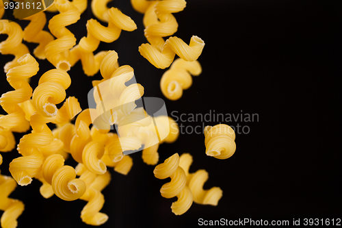 Image of Falling cavatappi pasta. Flying yellow raw macaroni over black background. 