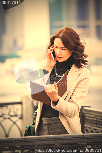 Image of businesswoman looking in a notebook and talking on mobile phone