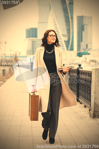 Image of woman in a light overcoat with a wooden case and a notebook